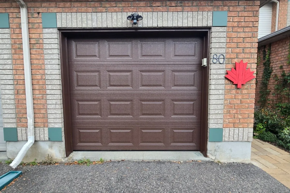 Brown brick Fallingbrook home with a brown insulated steel garage door under mature trees